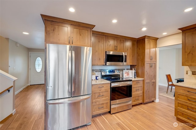 kitchen with stainless steel appliances, light wood-type flooring, light stone counters, and tasteful backsplash