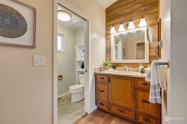 bathroom with vanity, wooden walls, hardwood / wood-style flooring, and toilet