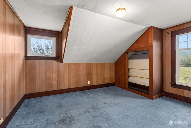 additional living space featuring wooden walls, light colored carpet, and lofted ceiling