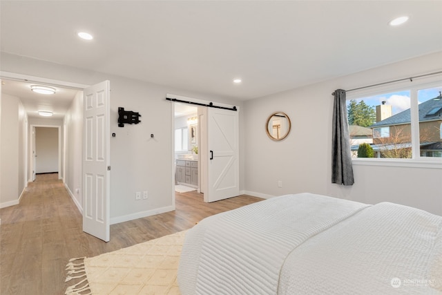 bedroom featuring ensuite bath, light hardwood / wood-style floors, and a barn door