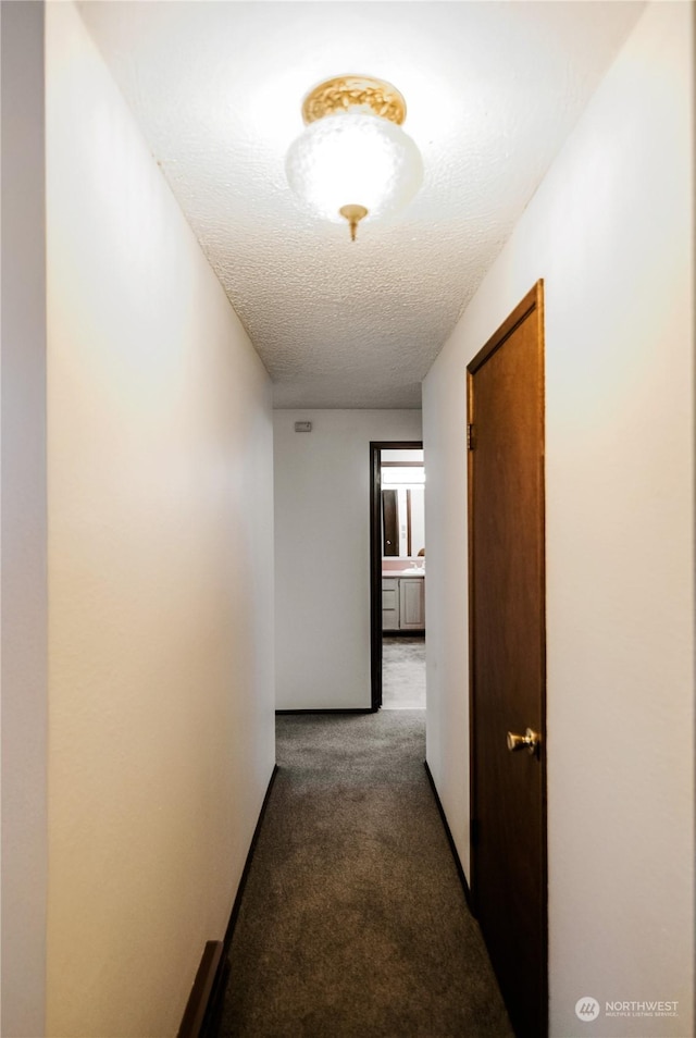 corridor with dark carpet and a textured ceiling