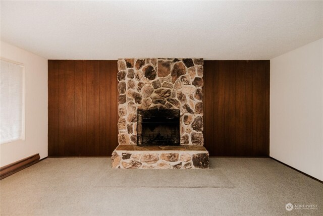 unfurnished living room featuring a stone fireplace, wooden walls, and light colored carpet