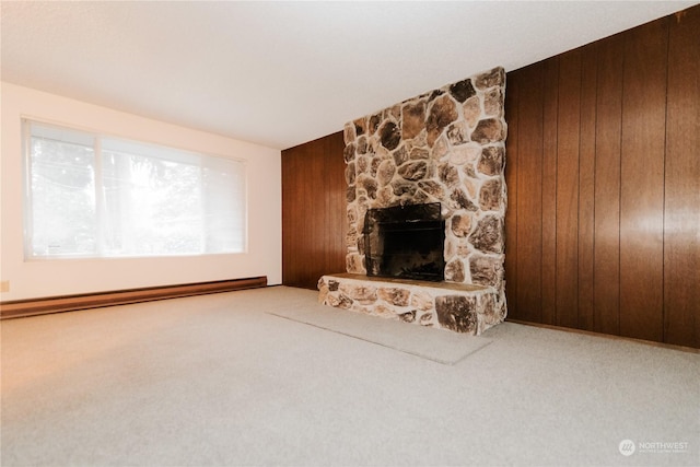 unfurnished living room with carpet flooring, wood walls, a stone fireplace, and a baseboard radiator