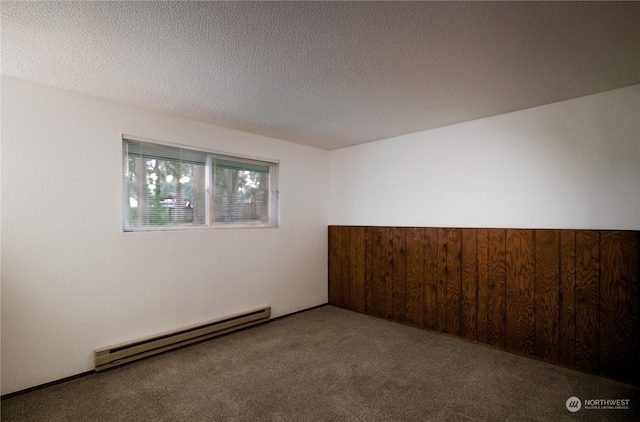 spare room featuring carpet flooring, wood walls, a textured ceiling, and a baseboard radiator