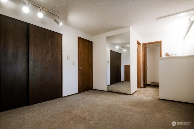 unfurnished bedroom with light carpet, a textured ceiling, and a baseboard radiator