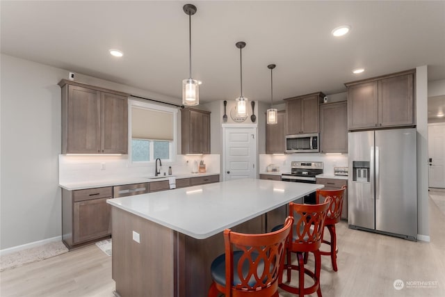 kitchen with stainless steel appliances, light hardwood / wood-style floors, decorative backsplash, a kitchen island, and decorative light fixtures