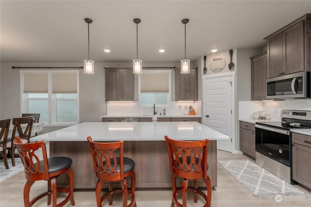 kitchen with light hardwood / wood-style flooring, appliances with stainless steel finishes, hanging light fixtures, a center island, and decorative backsplash