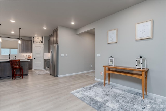 interior space with pendant lighting, a breakfast bar area, stainless steel fridge, dark brown cabinetry, and light wood-type flooring