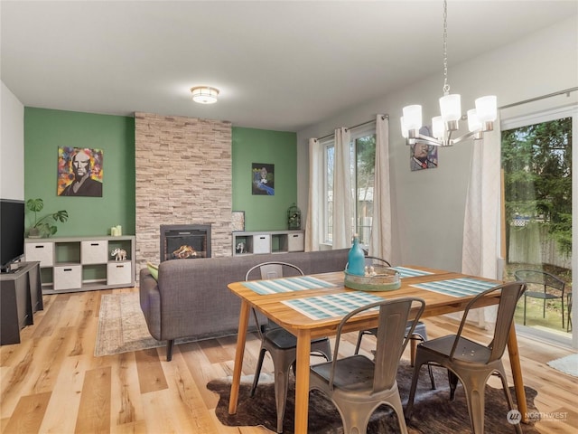 dining area with a stone fireplace, a notable chandelier, and light wood-type flooring