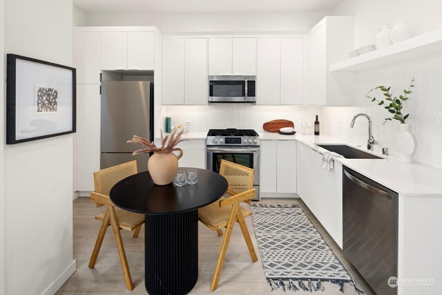 kitchen with backsplash, white cabinets, sink, light hardwood / wood-style flooring, and stainless steel appliances