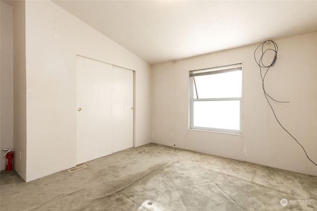 unfurnished bedroom with a closet, light colored carpet, and vaulted ceiling