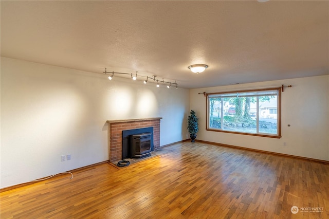 unfurnished living room with wood-type flooring, rail lighting, a textured ceiling, and a wood stove