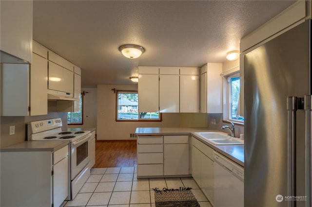 kitchen featuring white appliances, a textured ceiling, light tile patterned floors, white cabinets, and sink