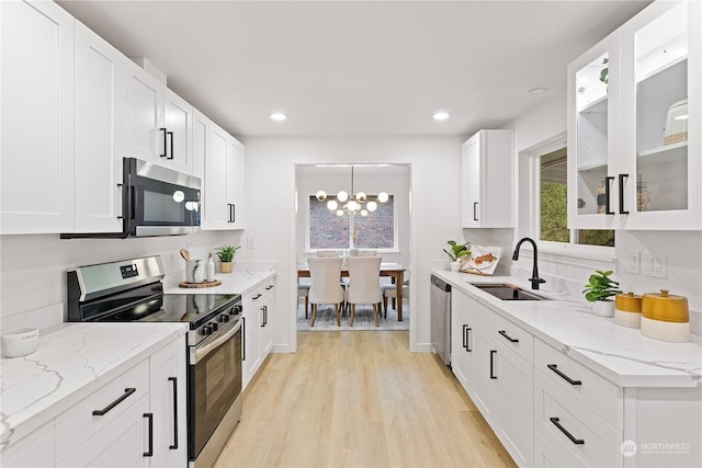 kitchen with light stone countertops, appliances with stainless steel finishes, sink, a notable chandelier, and white cabinets