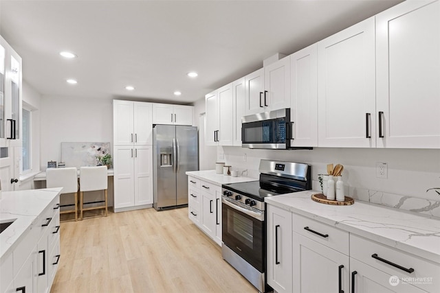 kitchen with light stone countertops, white cabinets, light wood-type flooring, and appliances with stainless steel finishes