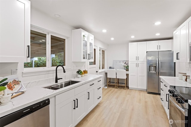 kitchen with white cabinetry, sink, light stone counters, and appliances with stainless steel finishes