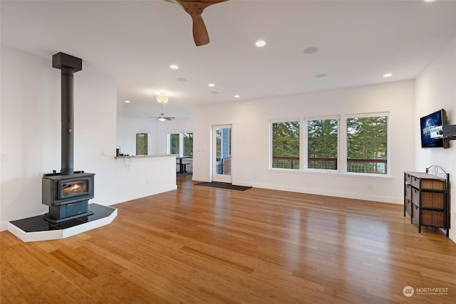 unfurnished living room with hardwood / wood-style flooring, a wood stove, and ceiling fan