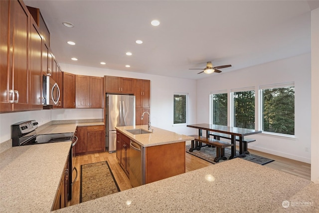 kitchen featuring ceiling fan, sink, light stone countertops, a kitchen island with sink, and appliances with stainless steel finishes