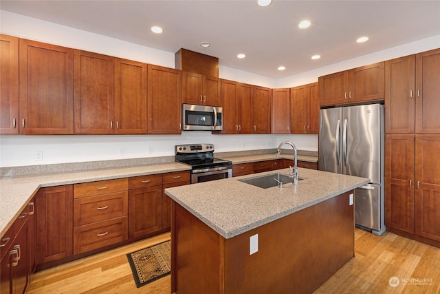 kitchen featuring light stone countertops, stainless steel appliances, a kitchen island with sink, sink, and light hardwood / wood-style flooring