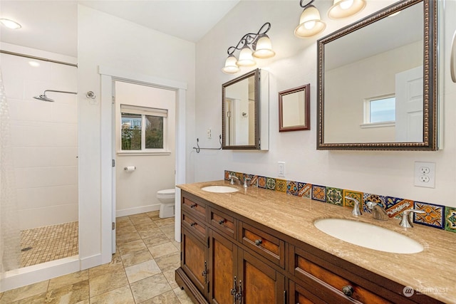 bathroom with a tile shower, vanity, toilet, and plenty of natural light