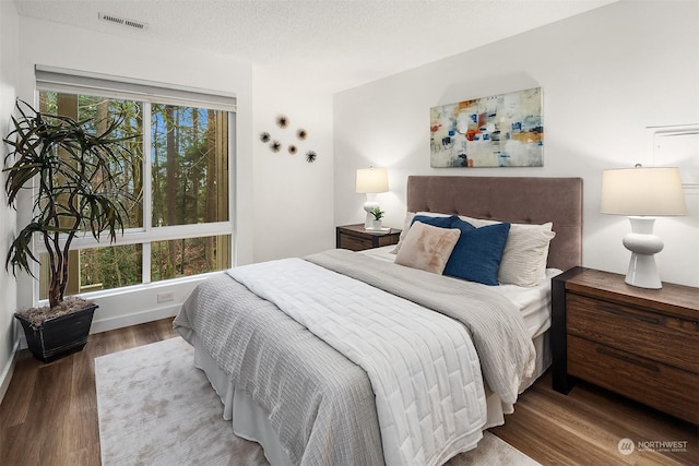 bedroom with a textured ceiling, dark hardwood / wood-style flooring, and multiple windows