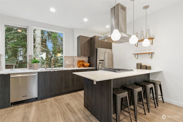 kitchen with sink, stainless steel appliances, island exhaust hood, pendant lighting, and decorative backsplash