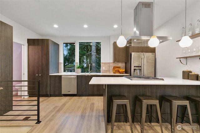 kitchen with stainless steel appliances, backsplash, island exhaust hood, kitchen peninsula, and light wood-type flooring