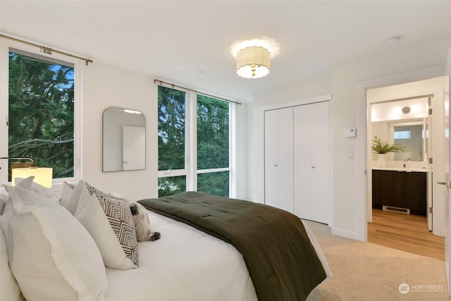 bedroom featuring ensuite bathroom, sink, and light colored carpet