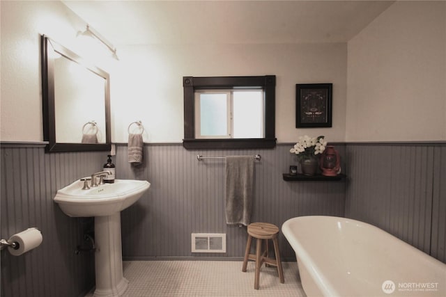 bathroom featuring a freestanding tub, a wainscoted wall, a sink, and visible vents