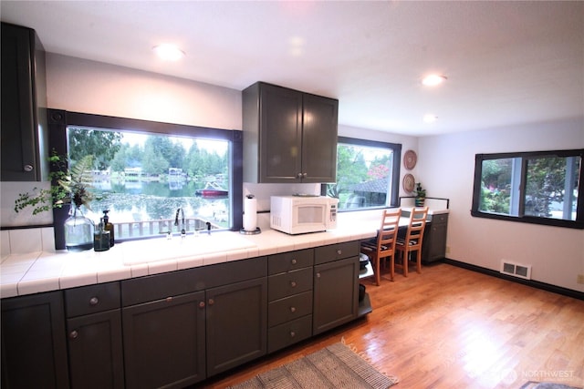 kitchen featuring tile counters, visible vents, white microwave, light wood-style floors, and a sink