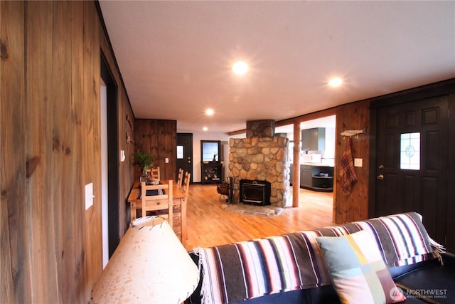 living room with light wood-type flooring, a wood stove, wooden walls, and recessed lighting