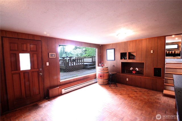 interior space with a baseboard heating unit, wood walls, and a textured ceiling