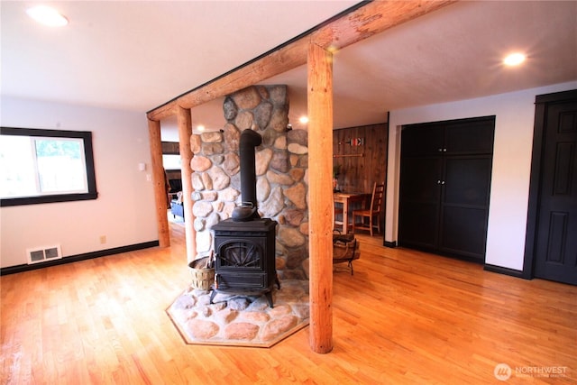 unfurnished living room featuring baseboards, visible vents, a wood stove, light wood-type flooring, and beam ceiling