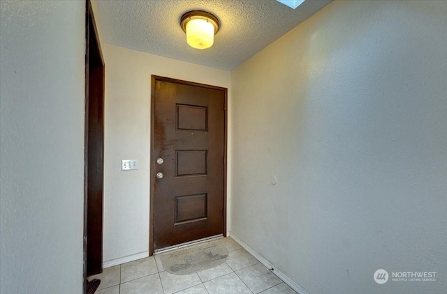 doorway featuring light tile patterned floors, a textured ceiling, and baseboards