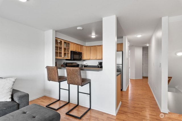 kitchen featuring kitchen peninsula, light hardwood / wood-style flooring, stove, and a breakfast bar