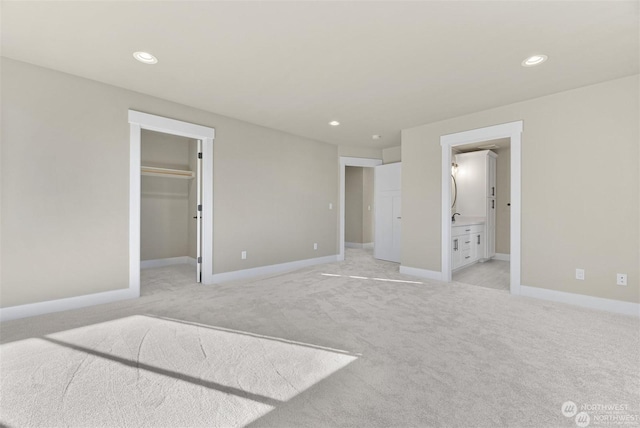 unfurnished bedroom featuring light carpet, a walk in closet, and ensuite bath