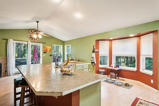 kitchen featuring a kitchen island with sink, sink, vaulted ceiling, light hardwood / wood-style floors, and a kitchen bar