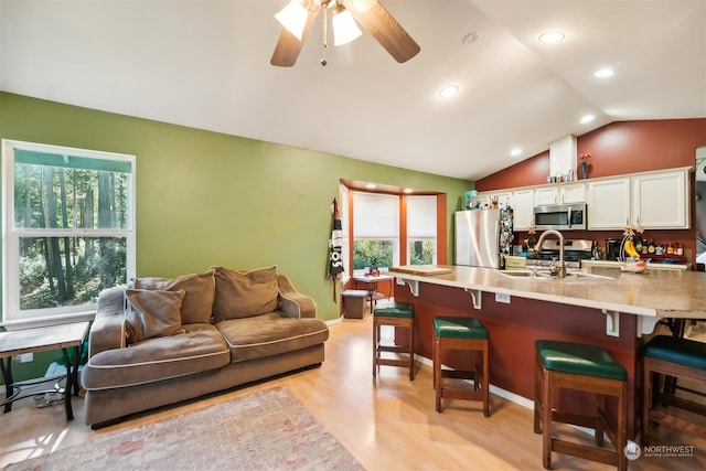 kitchen with white cabinets, a kitchen breakfast bar, stainless steel appliances, and light hardwood / wood-style flooring