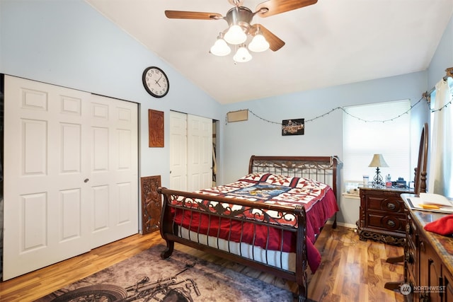 bedroom featuring hardwood / wood-style floors, two closets, vaulted ceiling, and ceiling fan