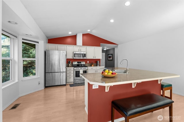 10405 Olympic Pl, Anderson Island, WA 98303 - kitchen featuring vaulted ceiling, a kitchen breakfast bar, a sink, white cabinetry, and appliances with stainless steel finishes