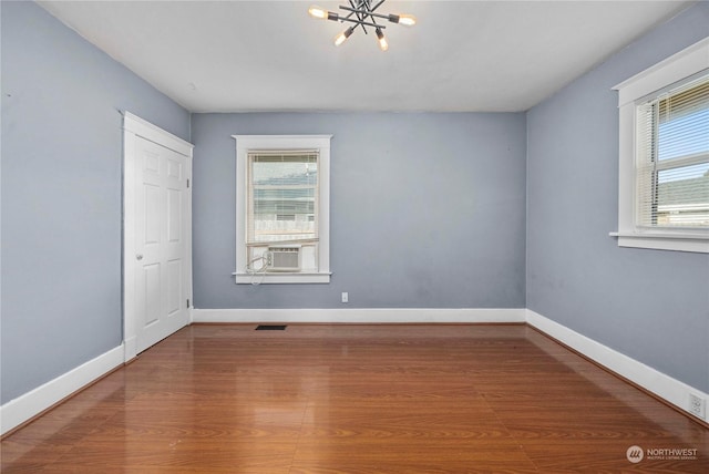 empty room featuring a notable chandelier and wood-type flooring