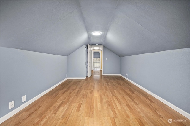 bonus room featuring a textured ceiling, lofted ceiling, and light wood-type flooring