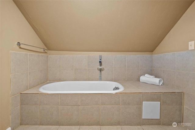 bathroom with tiled bath, vaulted ceiling, and tile patterned floors