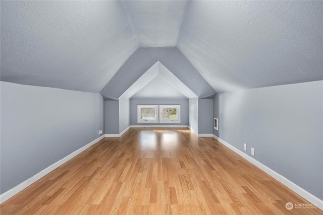 additional living space featuring a textured ceiling, light hardwood / wood-style flooring, and vaulted ceiling