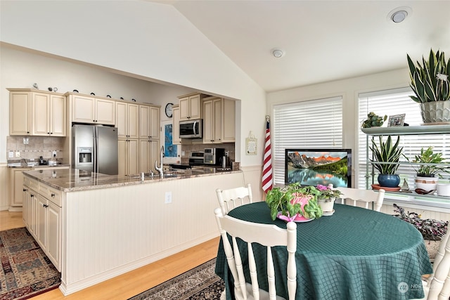 kitchen featuring light stone countertops, backsplash, stainless steel appliances, cream cabinets, and lofted ceiling