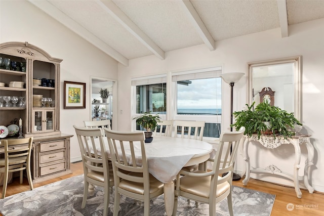 dining area with lofted ceiling with beams, a water view, wood-type flooring, and a textured ceiling