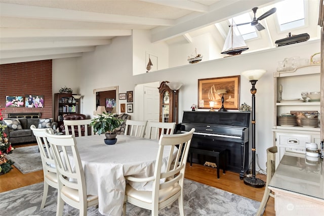 dining area with hardwood / wood-style floors, ceiling fan, lofted ceiling with skylight, and a brick fireplace