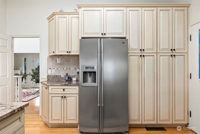 kitchen featuring stainless steel fridge, light wood-type flooring, backsplash, light stone counters, and cream cabinetry