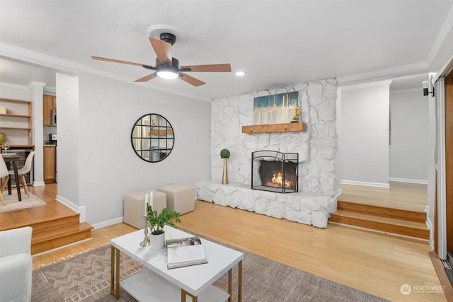 living room with light hardwood / wood-style flooring, ceiling fan, ornamental molding, and a stone fireplace