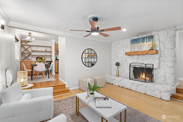 living room featuring ceiling fan, wood-type flooring, ornamental molding, and a fireplace